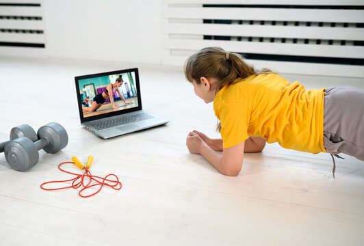 Young girl watching video online on laptop and doing plank fitness exercises at home. Distant training with personal trainer. Online education concept