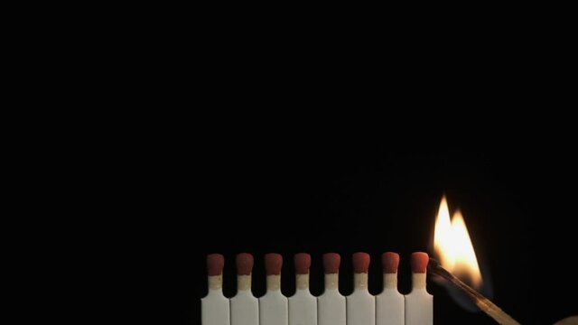 Slow motion. A match sets fire to a row of matches. Slow motion ignition of matches on a black background.