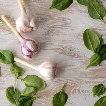 fresh garlic and spinach leaves on a light wooden table