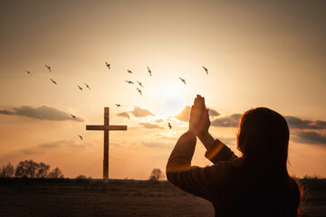 Woman praying against the background of a sunny sunset .