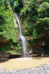 High wonderful waterfall falling from the rocks in beautiful southern forest.