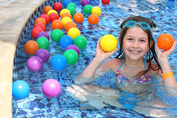 Girl having fun In garden paddling pool with color balls