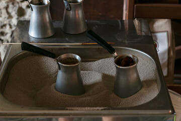 Process of preparation traditional turkish coffee in hot sand. Two metal pots with coffee are heating in sand.