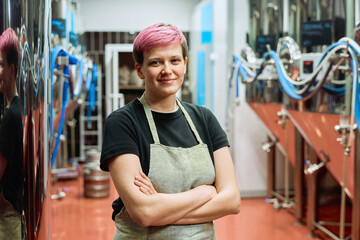 Young smiling blond female worker of beer production factory in workwear crossing arms by chest...