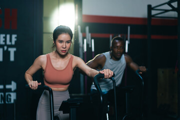 Fototapeta na wymiar Multi ethnic group of young athletes training on stationary bike cardio machine building muscle in fitness gym.
