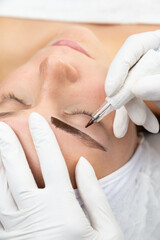 Kosmetolog wykonuje makijaż permanentny brwi, tatuaż na twarzy kobiety. Zbliżenie na proces pigmentacji brwi.  - obrazy, fototapety, plakaty