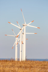 Wind turbines farm against a clear sunset sky with sea in background