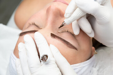 Kobieta w salonie urody. Makijaż permanentny brwi, proces tatuowania skóry. Twarz kobiety w trakcie zabiegu makijażu permanentnego. 