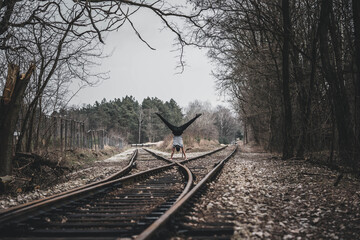 Young guy standing in his arms on the railroad rails