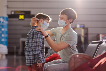 Parent wearing on child's protective mask at the airport. Travel to the coronavirus pandemic. New normal lifestyle. Father and son are waiting for departure in the lounge. Safety social distance