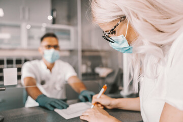 Obraz premium Attractive male lab assistant standing in hall of laboratory and giving form to a patient. She is gonna be tested for corona virus.