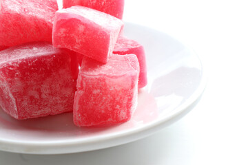 Red Turkish delights with sugar powder on plate on white table background. Oriental dessert sweet candy rahat locum. Top view, copy space