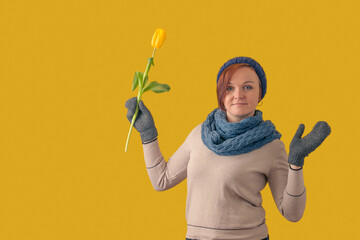 woman in a hat and mittens with a tulip flower spread her arms to the sides on a yellow background
