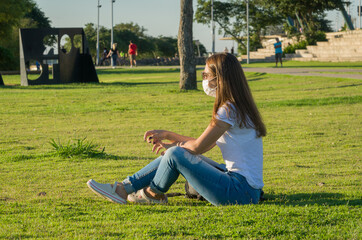 Young woman sitting on the grass with a protective mask during the SARS CoV-2 pandemic season (COVID 19)