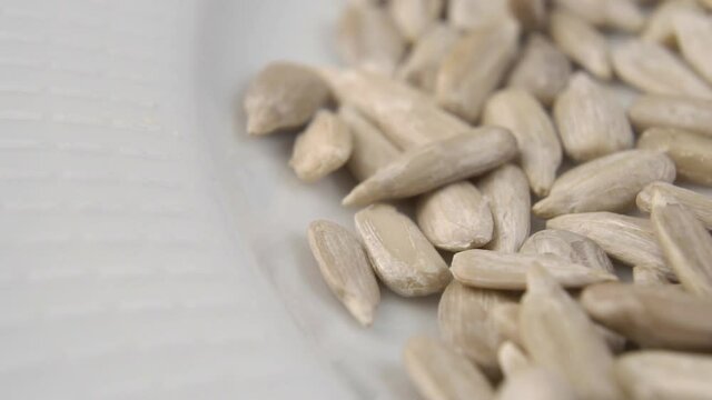 Raw peeled sunflower seeds fall in slow motion into a white plate. Macro. Dolly Shot