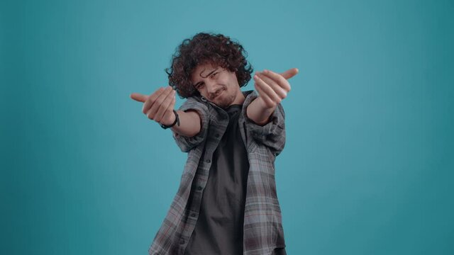 Cute and excited young hipster, with his hands he wants to hug smiling. Boy dressed in gray plaid shirt, on blue studio background The concept of people's lifestyle