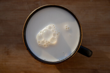 Glass of milk standing on old wooden table. Black glass with white milk. Black glass with white...