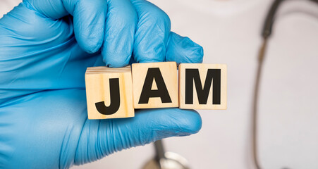 JAM - word from wooden blocks with letters holding by a doctor's hands in medical protective gloves. Medical concept.