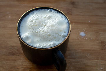 Glass of milk standing on old wooden table. Black glass with white milk. Black glass with white milk on the table