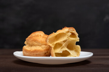 Profiteroles on close up on white saucer, black background. Preparation for eclairs.