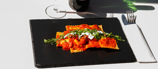 Four cheese filled ravioli in a tomato and basil sauce on the black stone plate