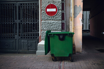 stop throwing out unsorted garbage. not an eco-friendly trash can. stop sign and green garbage container on the street. trash container near the house. old trash can without sorting.