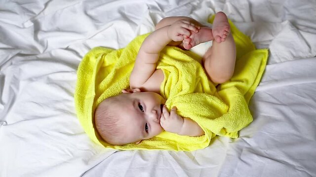 Cute toddler 5 months lies in bed after swimming in a yellow towel, view from above