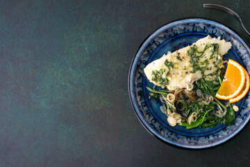 fried halibut with spinach and orange sauce on a blue plate on a dark table