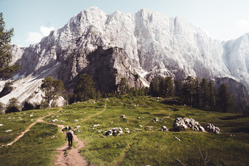 Young woman on the trail looking on high mountain peak at sunset in Dolomites, Italy. Autumn landscape with girl, path, rocks, sky with clouds at colorful sunset. Hiking in alps. Majestic mountains