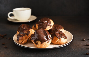 Profiteroles with vanilla cream and chocolate sauce with a cup of coffee on the kitchen table.