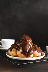 Profiteroles with vanilla cream and chocolate sauce with a cup of coffee on the kitchen table.