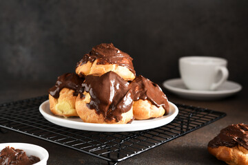 Profiteroles with vanilla cream and chocolate sauce with a cup of coffee on the kitchen table.