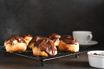 Profiteroles with vanilla cream and chocolate sauce with a cup of coffee on the kitchen table.