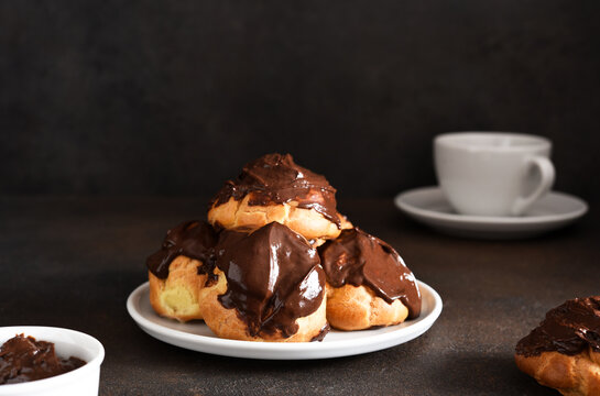 Profiteroles with vanilla cream and chocolate sauce with a cup of coffee on the kitchen table.