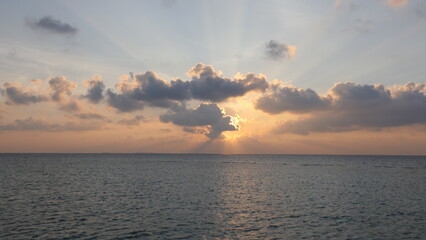 Sunset in the maldives with sun partly covered by clouds