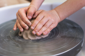 A child works with clay on a potter's wheel. The concept of a creative children's workshop.
