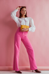 Elegant fashionable woman wearing white vintage blouse with lace collar, pink jeans, holding small...
