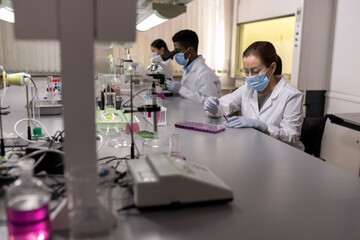 Obraz premium Young chemist in protective mask sitting at the table and working with chemical samples in the lab