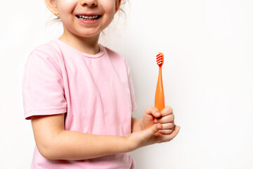 a small blonde girl smiles and holds a toothbrush on a white background, a place for text, the concept of caring for children's baby teeth and oral hygiene