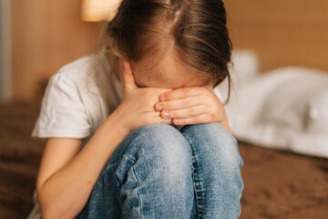 Close-up of disappointed little girl hugging knee, sobbing with head bowed and crying sitting on...