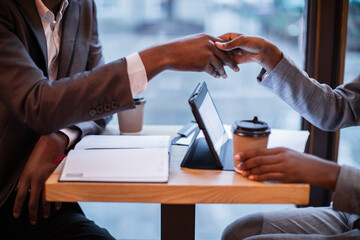 Close up of afro american business people shaking hands for concluding bargain while sitting at...