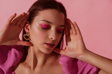 Close up beauty portrait of young beautiful woman with pink, fuchsia color eyeshadow makeup, flawless clean skin, wearing elegant golden earrings, pink blouse. Spring, summer fashion trend - obrazy, fototapety, plakaty