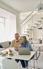 Senior mature couple check bank loan documents using laptop at home. Middle aged old family read...