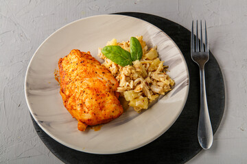 Baked chicken breast with salad on a plate decorated with spinach next to a fork on a gray background on a round black stand.