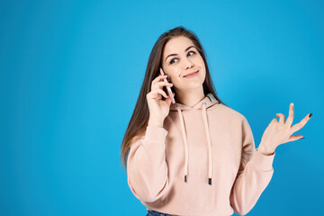 A young girl is talking on the phone. Portrait of emotions - happy and smile, got good news. Isolated on a blue background.