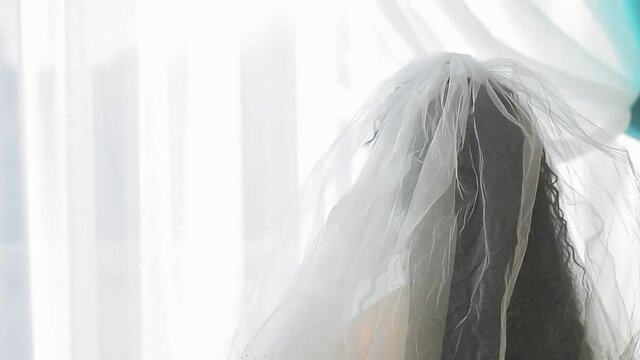 A Jewish bride in a wedding dress and veil wearing a medical mask in a synagogue hall before the chupah ceremony speaks on the phone