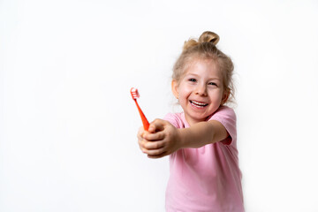 a cheerful little blonde girl smiles and holds a toothbrush on a white background, a place for text, the concept of caring for children's baby teeth and oral hygiene