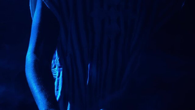 Silhouette of african american man playing piano synthesizer on stage in dark smoky studio. Black musician with white ethnic pattern on his face performs against background of blue lights. Close up.