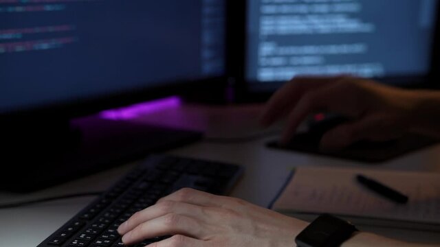 Young programmer works in front of computer typing on keyboard and writing notes in macro. A caucasian male is doing his job in IT sphere. He is coding new software. Cyberspace and modern technologies