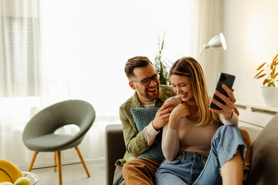 Excited Couple Relax On Couch Feel Euphoric Win Lottery Online On Cellphone.